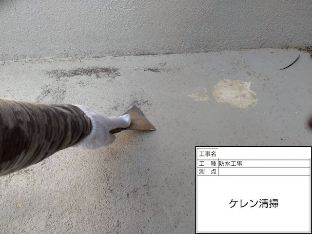 防水層の密着を良くするためのケレン清掃作業。ヘラを使って床面の汚れや脆弱部を除去している様子。